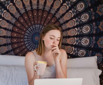teen on her bed with cup of coffee and tapestry as a headboard reviews her checking account SheeksFreaks Financial Skills for Young Adults