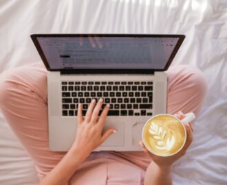 young woman sits on her bed with coffee while she manages her checking account SheeksFreaks Financial Skills for Young Adults
