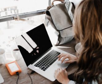 young woman sits at a contemporary looking cafe while working on her laptop SheeksFreaks Financial Skills for Young Adults